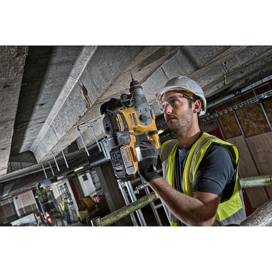 Worker using a DEWALT DCH283NT power tool to drill into a ceiling on a construction site.