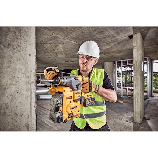 Worker uses a DEWALT DCH335X2 rotary hammer drill on a concrete wall at a construction site.