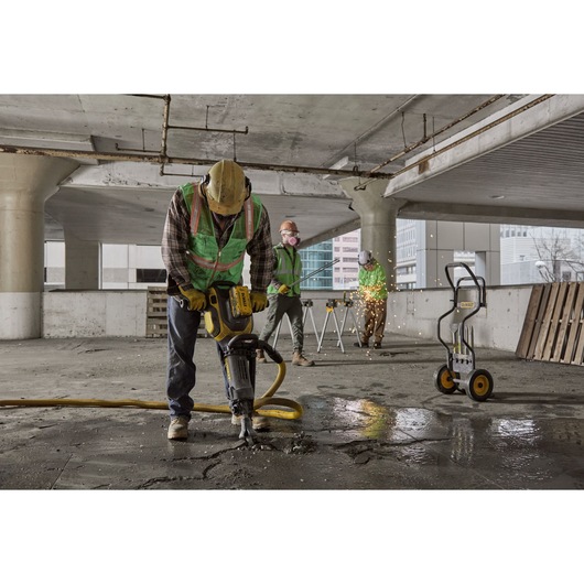 Workers use DEWALT tools for construction in a concrete building, including a jackhammer and equipment cart.