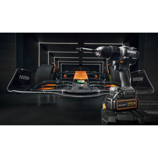 A DEWALT cordless power drill is displayed in the foreground with a black and orange formula race car in the background, set inside a modern, illuminated garage.