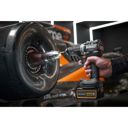 A DEWALT cordless drill being used to work on the wheel area of a racing car, with the drill prominently showing its branding and specifications.