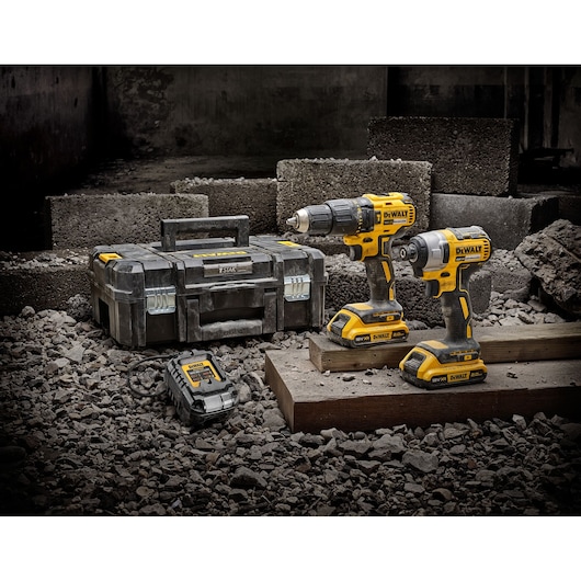 DEWALT tool set with two cordless drills, charger, and a toolbox on a construction site with rubble.