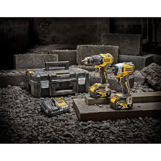 Two DEWALT cordless drills, charger, and case on rough construction site with concrete blocks and gravel.