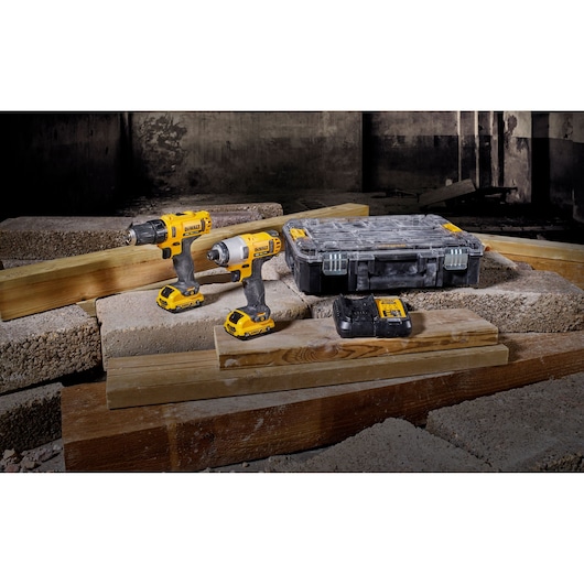 Two DEWALT cordless drills, battery, and case displayed on wooden planks and concrete blocks in a construction setting.