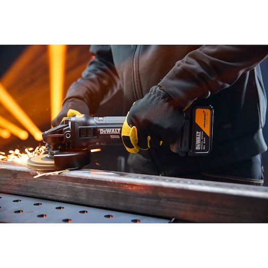 A person uses a DEWALT cordless grinder on metal, producing sparks. They wear gloves and a dark jacket.