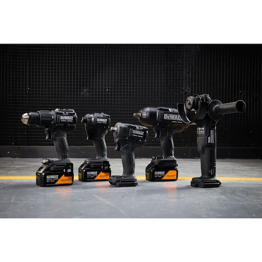 Four DEWALT black cordless power tools with batteries are lined up on a gray floor in front of a black wall.