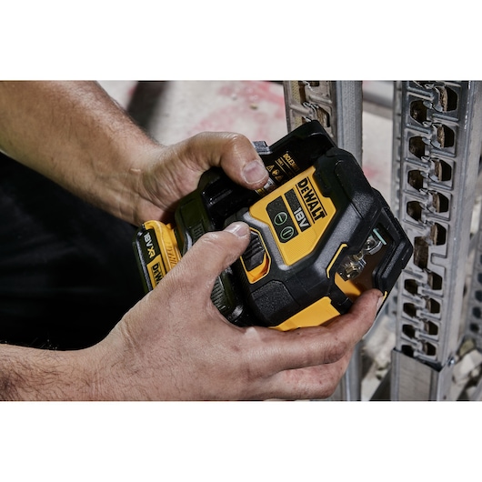 Hands adjusting a DEWALT 18V XR laser level near a metal framework at a construction site.