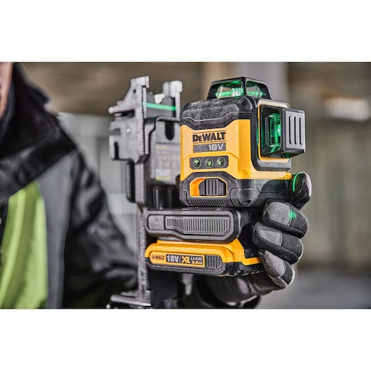 A close-up of a person holding a DEWALT 18V green laser level tool with rechargeable lithium-ion battery, suitable for construction or photography alignment tasks.