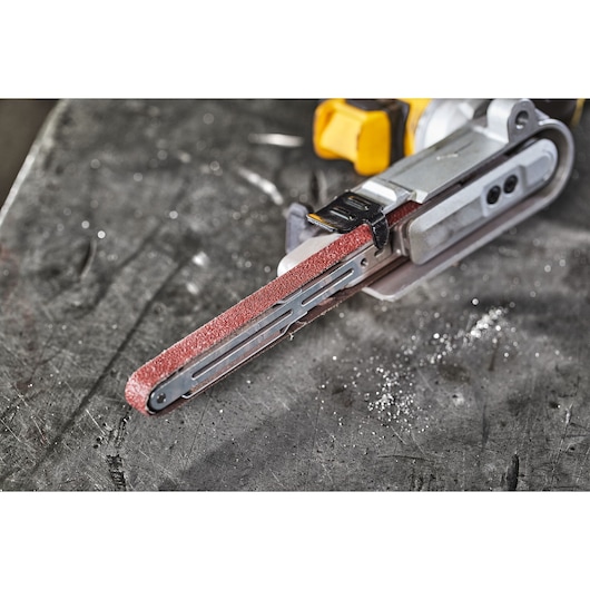 Close-up of a DEWALT cordless file sander with abrasive belt, resting on a metal work surface.
