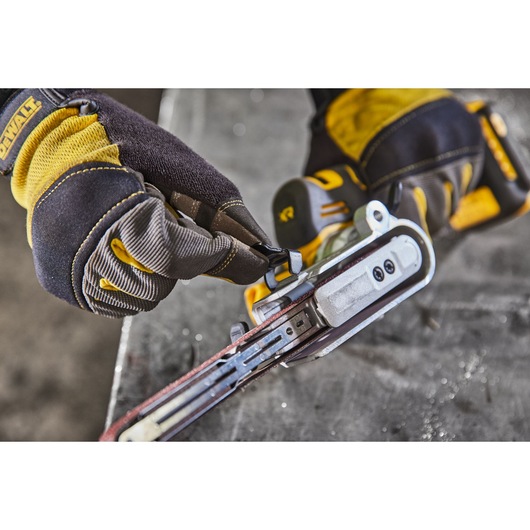Gloved hands adjust a DEWALT DCM200NT power tool, focusing on the sanding belt mechanism.