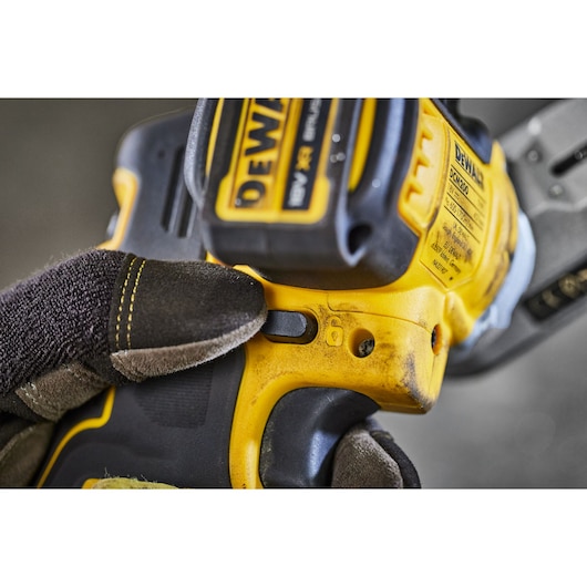Gloved hand pressing a button on a yellow DEWALT cordless tool, model DCM200N, close-up view.