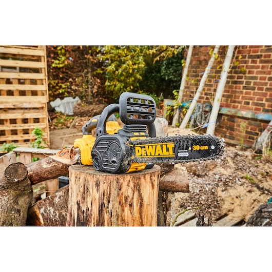 DEWALT chainsaw DCM565N with 30cm blade resting on a tree stump outdoors.