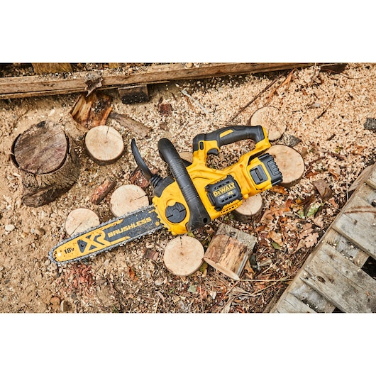 Dewalt cordless chainsaw on ground with cut wood and sawdust outdoors.