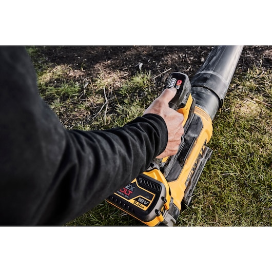 Person using a DEWALT 18V cordless leaf blower outdoors on grass.