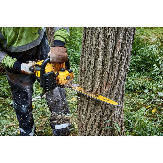 A person using a yellow DEWALT chainsaw to cut through a tree trunk outdoors, wearing protective gloves and clothing.