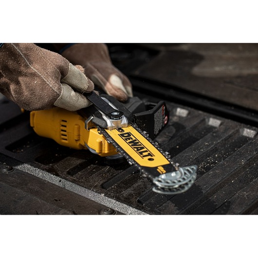 Gloved hands adjust the chain on a yellow DEWALT DCMPS520N pole saw, lying on a black textured surface.