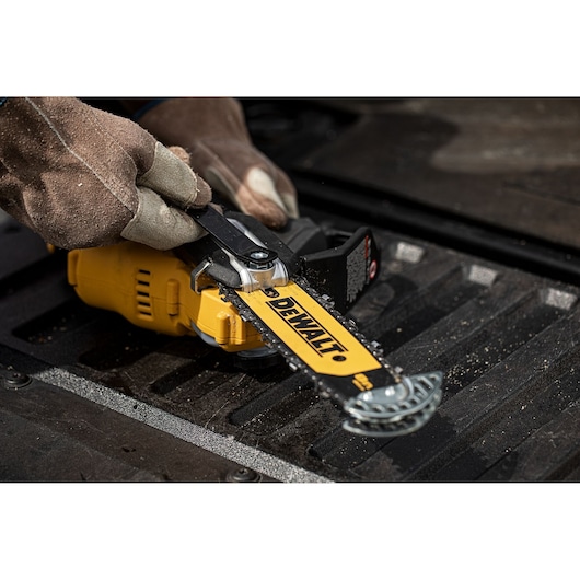 Gloved hands adjust a DEWALT chainsaw, model DCMPS520P1, lying on a dark textured surface.