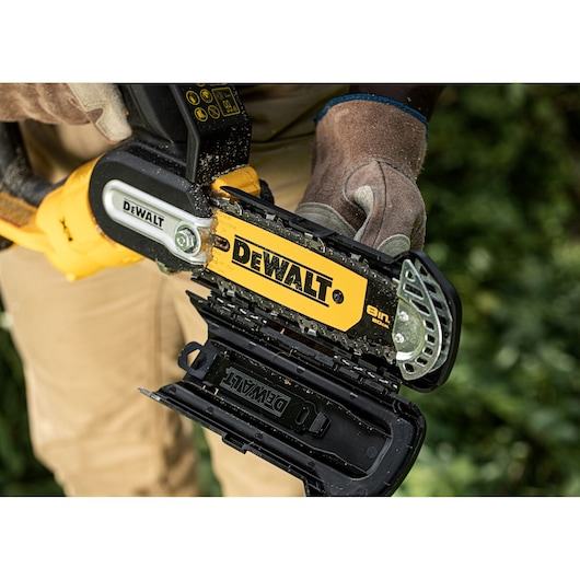 Close up of a DEWALT cordless pruner with chain guard being opened by gloved hands outdoors.