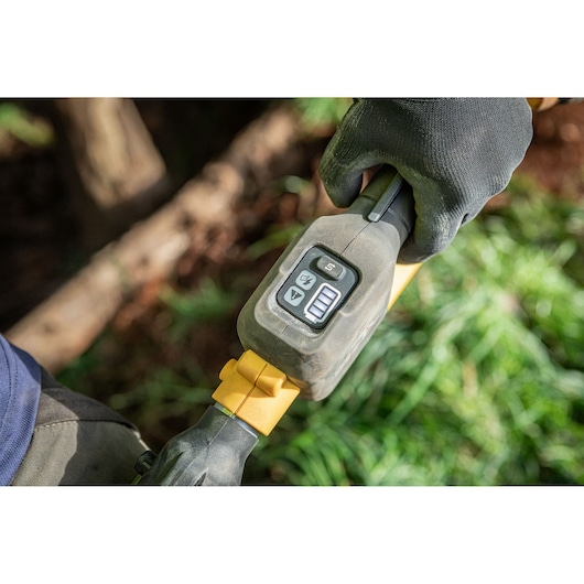 Gloved hand holding DEWALT tool handle with control buttons and display outdoors.