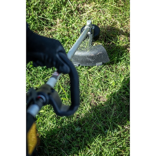 Close-up of a person using a DEWALT string trimmer to cut grass outdoors.