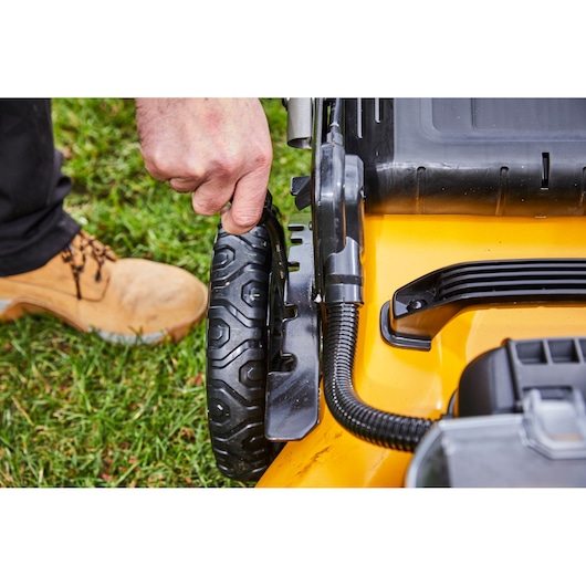 Hand adjusts the wheel height on a yellow DEWALT lawn mower outdoors.