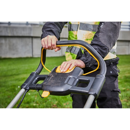 Person operating a DEWALT lawn mower, focusing on the handle and control panel outdoors.