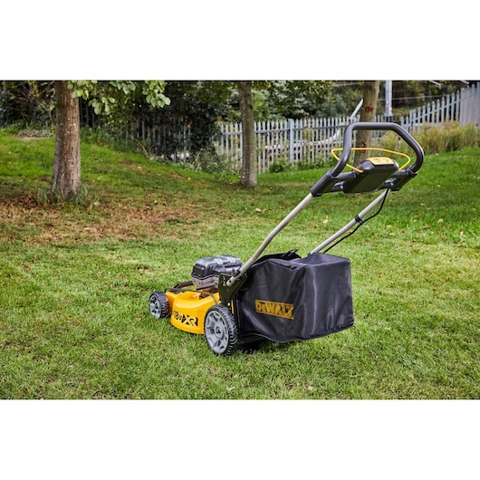 DEWALT yellow and black lawn mower on grass, with bag attached and trees in the background.
