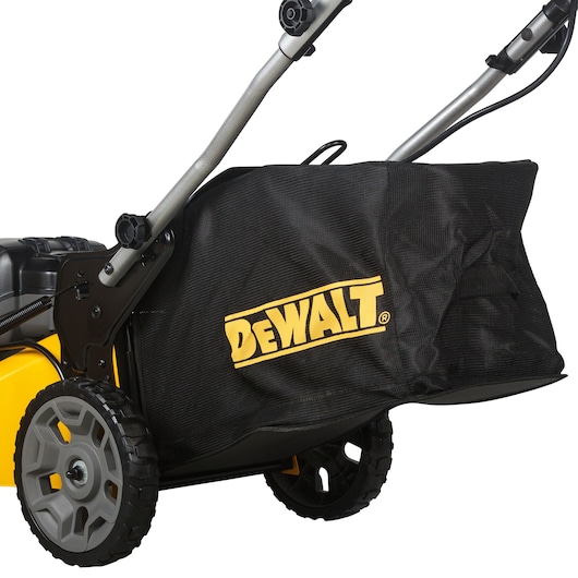 Close-up of a DEWALT lawn mower showing its wheels, handle, and a black grass collection bag with the DEWALT logo.