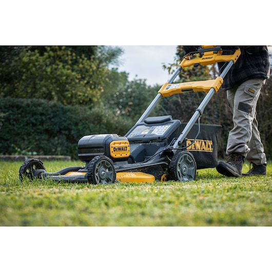 DEWALT battery-powered lawn mower in use outdoors by a person, close-up view of the mower and grass.