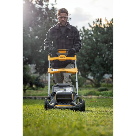 Person using a DEWALT lawn mower on grass outdoors, face obscured, trees in background.