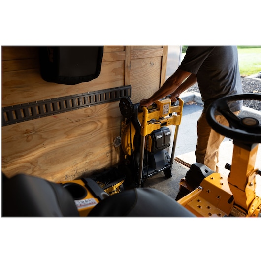 Person storing yellow DEWALT lawn mower upright in a shed with wooden walls.