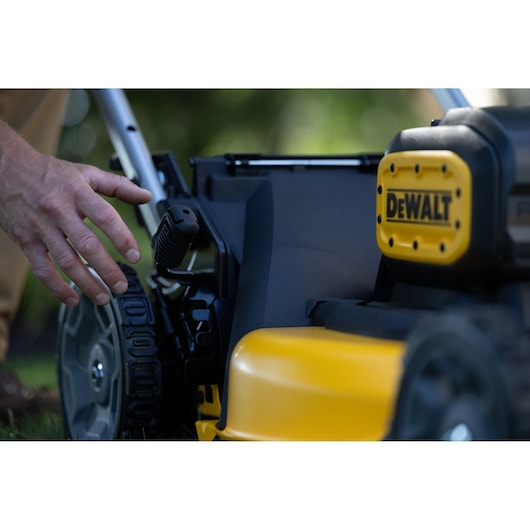 Close-up of a hand adjusting a lever on a yellow DEWALT lawn mower outdoors.