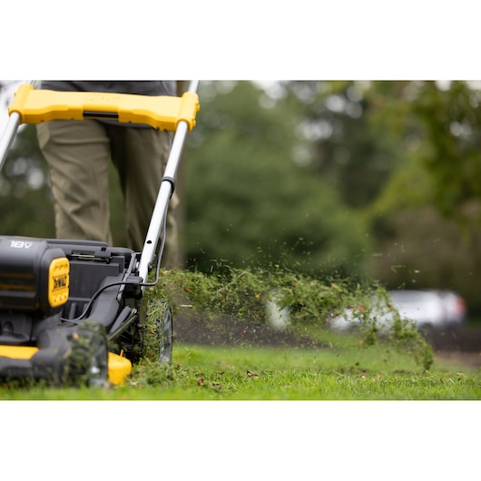 DEWALT lawn mower in use, ejecting grass clippings onto a lawn outdoors.