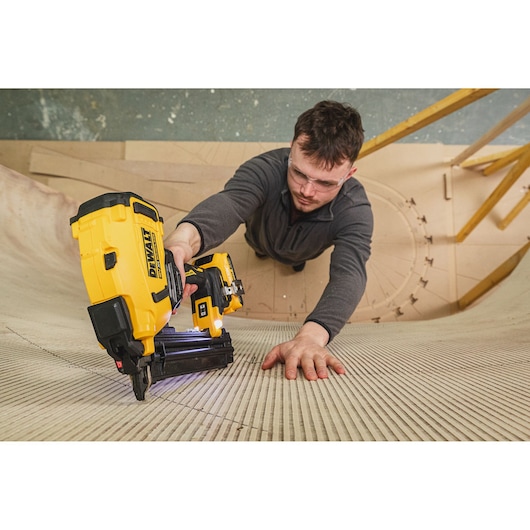Person using a DEWALT nailer on curved wooden surface, wearing safety glasses and gray top.