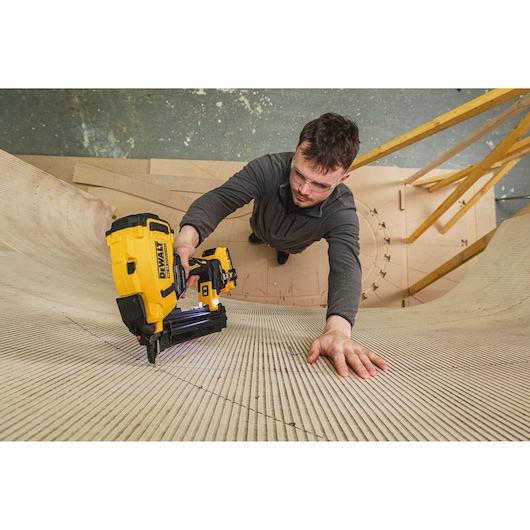 Person using a DEWALT DCN210SN-XJ nailer to fasten curved wood panels in a workshop setting.