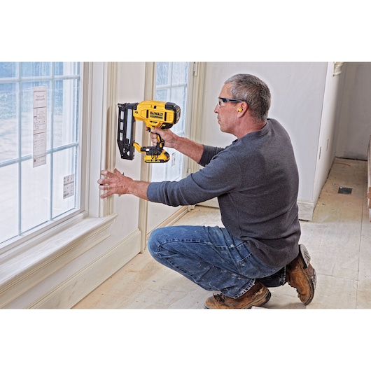 Person uses a DEWALT nailer to attach trim near a window during interior construction.