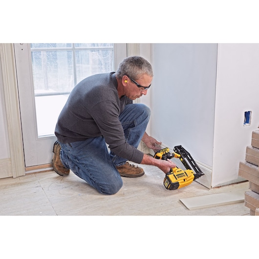 Person using a DEWALT nailer to attach baseboard near a door frame in a room under renovation.