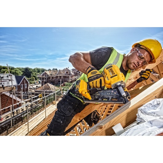 Worker uses a DEWALT cordless nailer DCN692N on a wooden roof frame at a construction site.