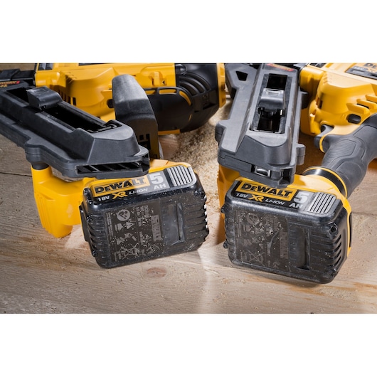 Two DEWALT 18V XR Li-Ion power tools with 5Ah batteries resting on a wooden surface with sawdust.