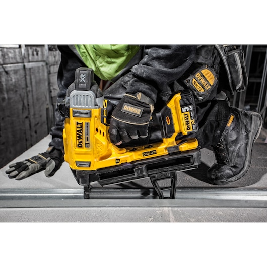 A DEWALT cordless concrete nailer model DCN890P2 being used by a person wearing protective gloves and clothing on a construction site.