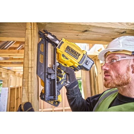DEWALT nail gun used on wood frame construction; person wearing safety gear, face obscured.