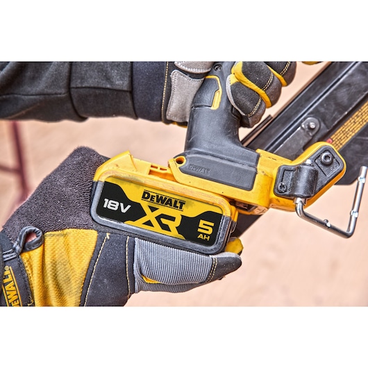Gloved hand holding a DEWALT 18V XR 5Ah cordless tool, close-up of battery and handle.