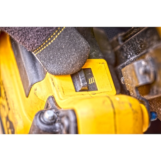Close-up of a gloved hand adjusting a yellow DEWALT tool switch.