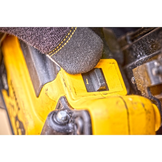 Gloved hand presses a yellow DEWALT tool control switch in a close-up, showing equipment details and texture.