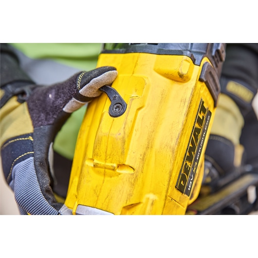 Close-up of a gloved hand adjusting a yellow DEWALT DCN930N tool with visible logo and textured surface.