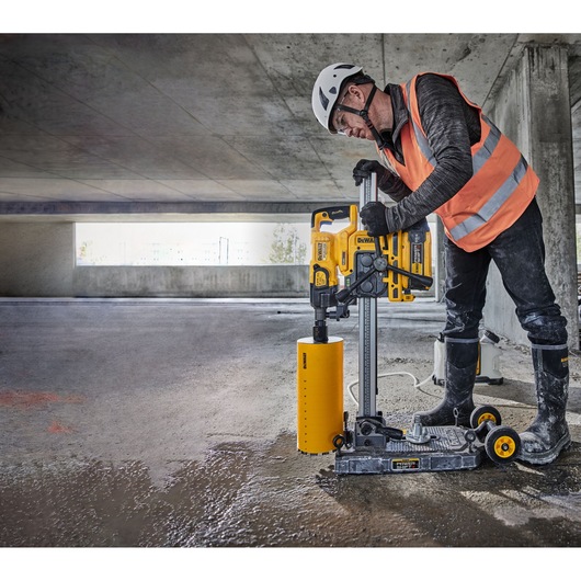 Worker uses DEWALT DCPS151 core drill on wet concrete in a parking structure, wearing safety gear.