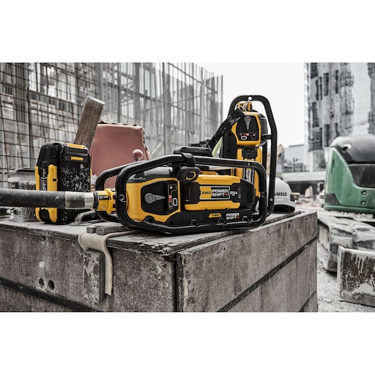 A DEWALT Power Shift DCPS320N battery-powered pole saw resting on a wooden surface at a construction site, with other DEWALT tools and building equipment visible in the background.