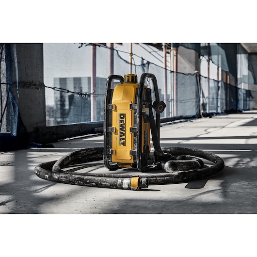 A DEWALT portable tool with a yellow body and black frame, featuring handles and a long flexible hose, placed on a concrete floor at a construction site.