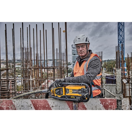 A construction worker wearing safety gear and an orange vest is holding a DEWALT Power Shift tool (model DCPS320N) at a building site, with reinforcement bars in the background.