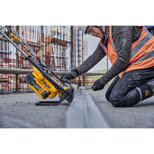 A person wearing construction safety gear uses a DEWALT cordless power tool (SKU: DCPS330N) on a metal beam at a construction site.